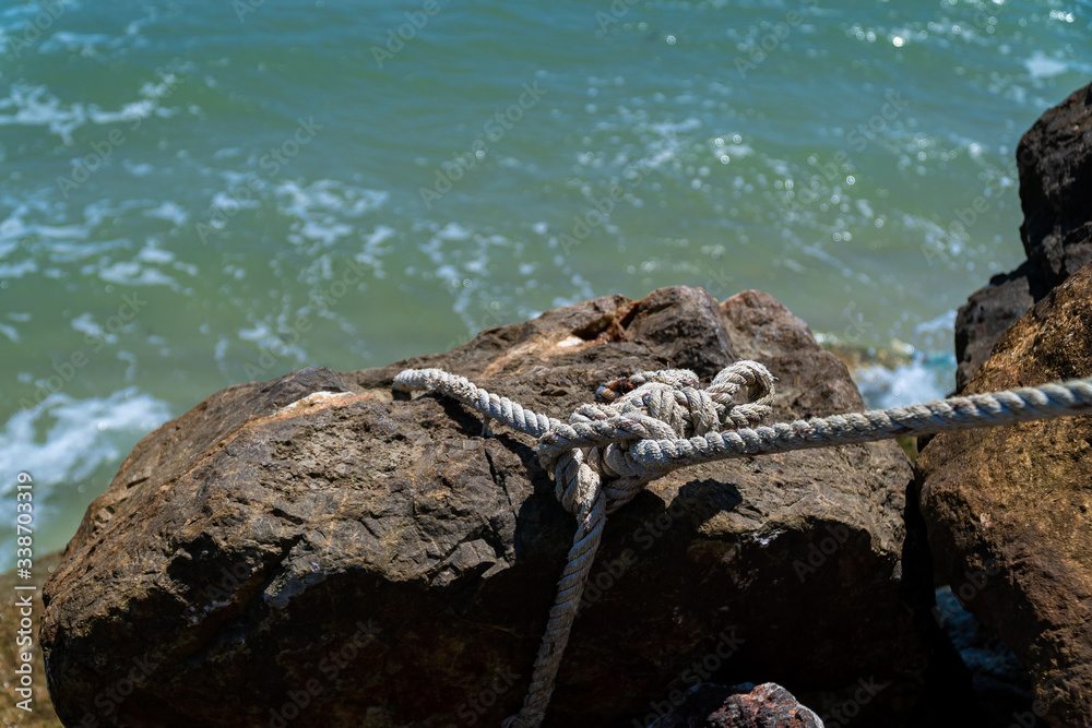 Copy space and shade. A rope tied with large stone for anchorage at the coast.