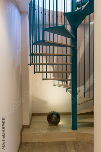 Fotografi Spiral staircase, forged blue handrail and wooden steps in modern home