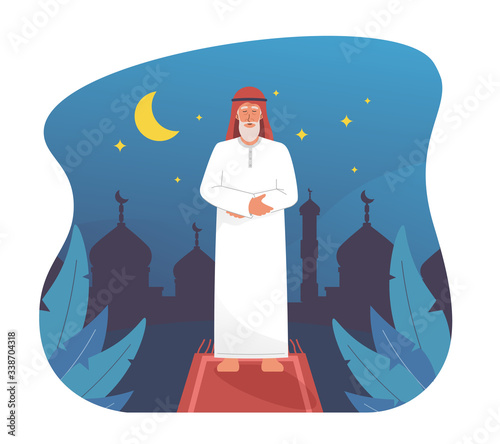 Muslim man praying at night with silhouette of mosque
