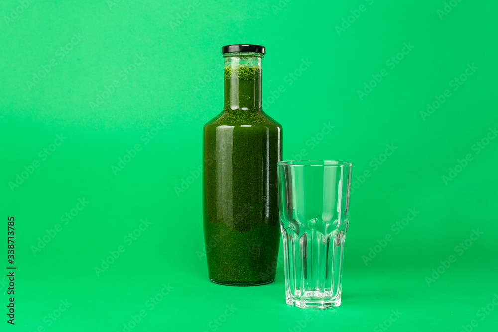 Fresh celery spinach juice in a glass bottle and an empty glass near isolated on green background. Healthy eating Detox juice diet. Fresh celery spinach juice in a glass bottle and an empty glass near isolated on green background. Healthy eating Detox juice diet.