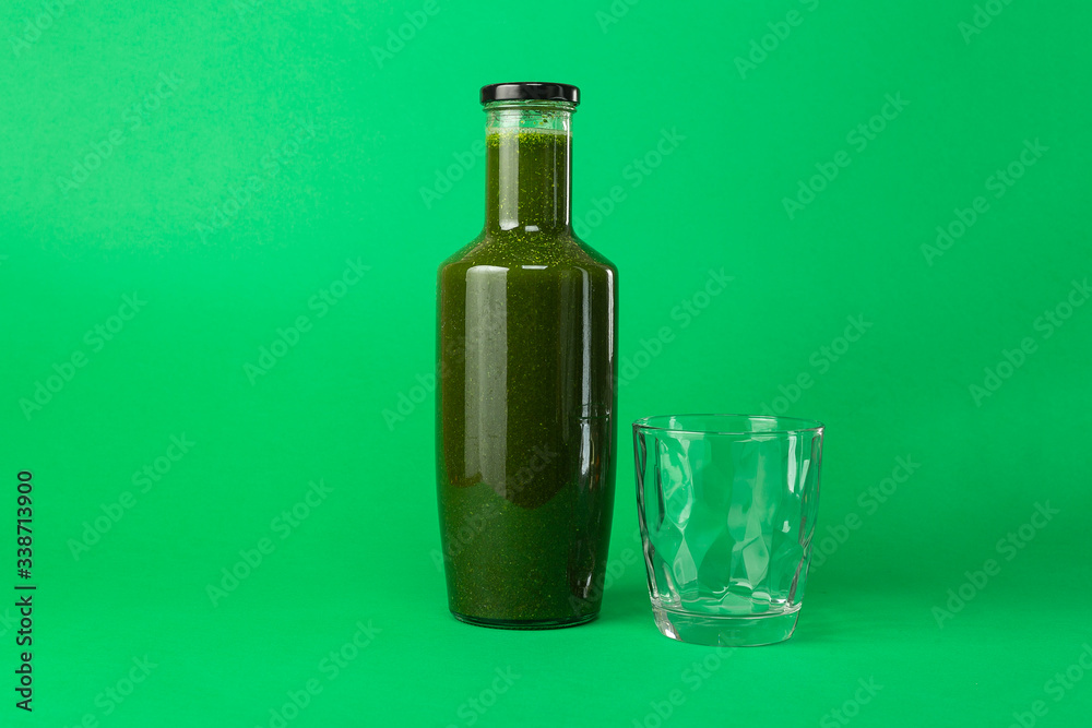 Fresh celery spinach juice in a glass bottle and an empty glass near isolated on green background. Healthy eating Detox juice diet.