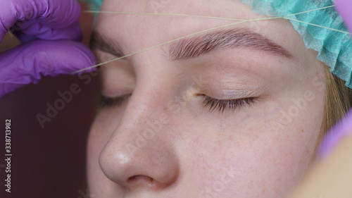 Close-up of female eye with thriding. Triding popular thread eyebrow correction technology. Eyebrow thriding - epilation procedure for brow shape correction. Plucking eyebrows and modeling. . photo