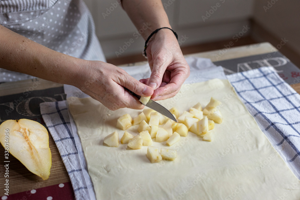 Female hands cutting a pear with a knife over a layer of puff pastry. Female hands cutting a pear with a knife over a layer of puff pastry.
