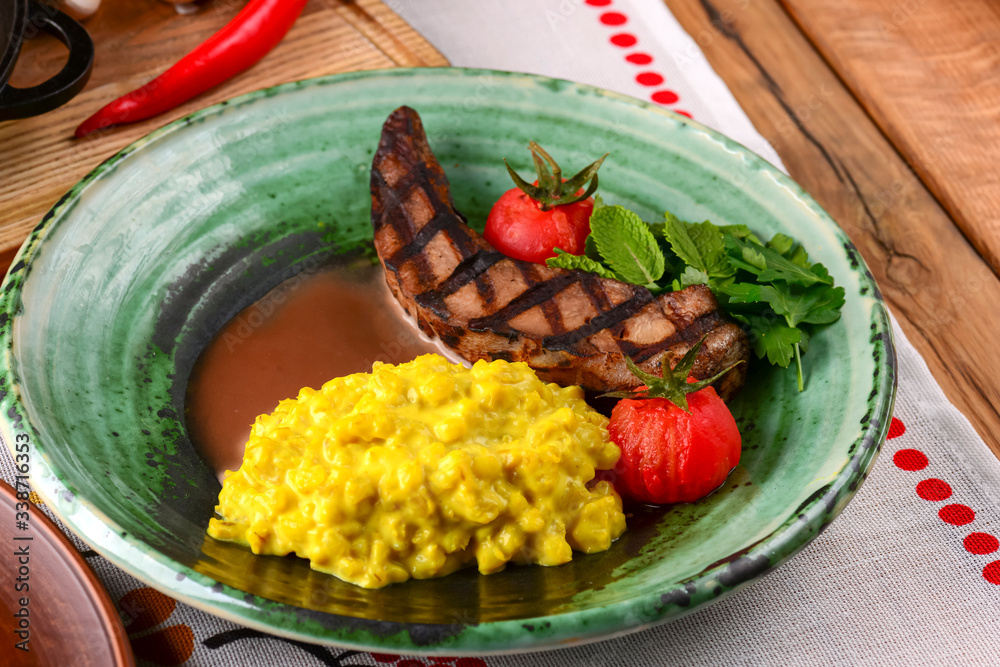 Grilled steak with gravy and vegetables served on a green plate over traditional Ukrainian tablecloth. Grilled steak with gravy and vegetables served on a green plate over traditional Ukrainian tablecloth.