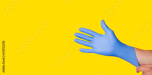 Hands wearing a blue latex glove, isolated on yellow background photo