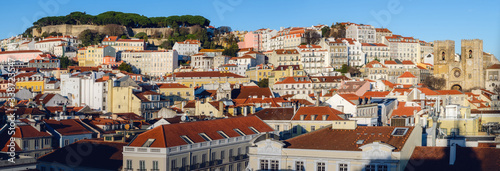 Sunset panorama of Alfama neighborhood in Lisbon, Portugal, with the famous castle of Sao Jorge on the hilltop and the cathedral of Santa Maria Maior bettween the tooftops