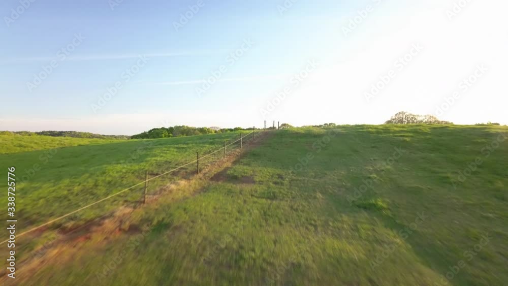 High speed aerial flight along the landscape and over a hill to reveal a heard of horses grazing in an idyllic green pasture