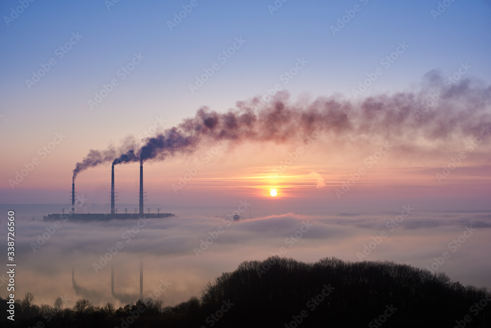 Colorful blue and pink sky with bright rising sun at thermoelectric power plant. Thermal chimneys producing dense smoke with toxic gases into atmosphere. Concept of ecology and environmental pollution