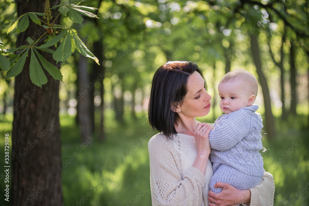 A beautiful mother holds her little son in her arms. A mother hugs her son - mother’s love and protection. A young woman with a child walks in the park. Life before and after the global pandemic. A beautiful mother holds her little son in her arms. A mother hugs her son - mother’s love and protection. A young woman with a child walks in the park. Life before and after the global pandemic.