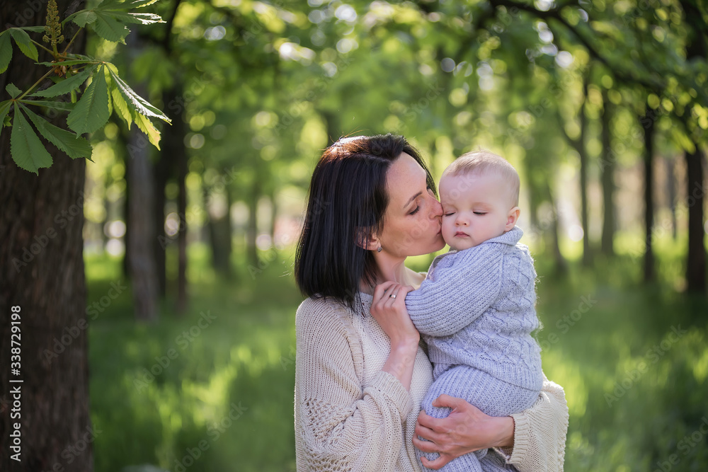 A beautiful mother holds her little son in her arms. A mother hugs her son - mother’s love and protection. A young woman with a child walks in the park. Life before and after the global pandemic. A beautiful mother holds her little son in her arms. A mother hugs her son - mother’s love and protection. A young woman with a child walks in the park. Life before and after the global pandemic.