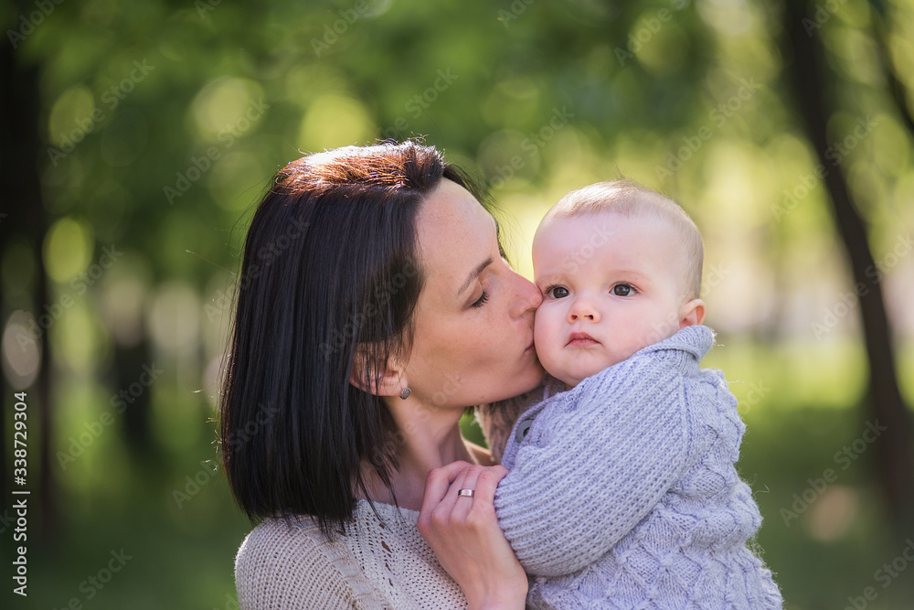 A beautiful mother holds her little son in her arms. A mother hugs her son - mother’s love and protection. A young woman with a child walks in the park. Life before and after the global pandemic. A beautiful mother holds her little son in her arms. A mother hugs her son - mother’s love and protection. A young woman with a child walks in the park. Life before and after the global pandemic.