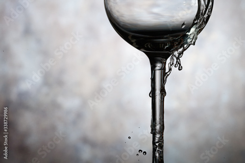 Motion of pouring splash water in transparent wine glass. Water splashing out of a tall wine glass.