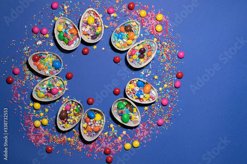 Halves of chocolate eggs with colored jelly and sweet powder form a circle on a blue background. The photo was taken fla tlay. There is a place for text. photo