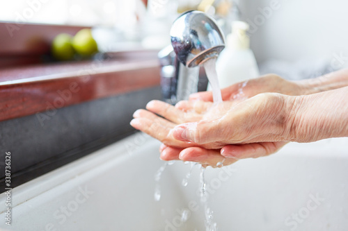 Old woman washing hands with soap under tap