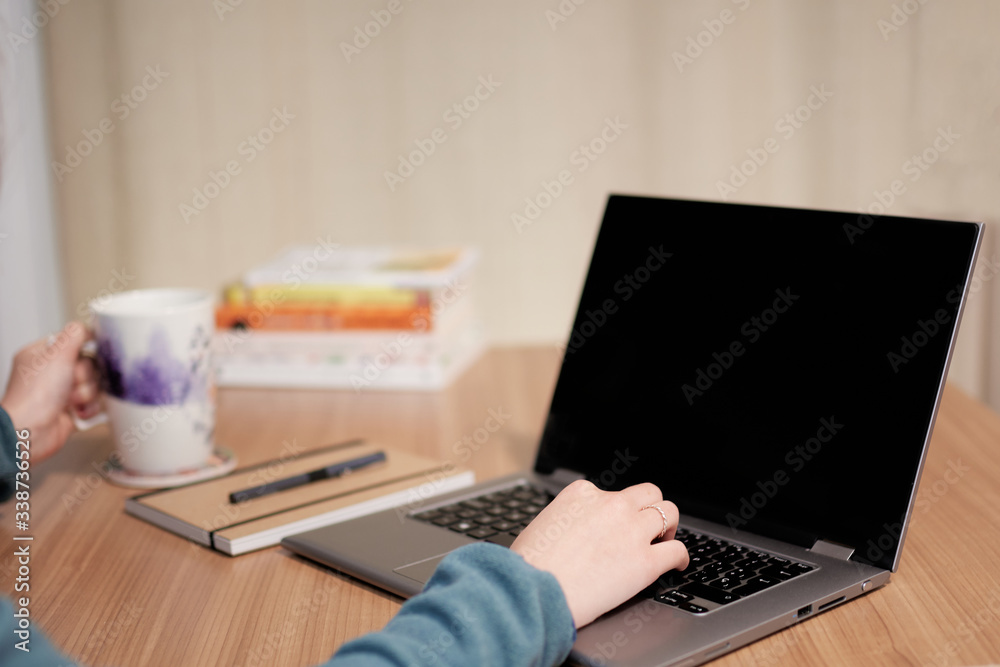 computer on a wooden table, one hand typing and the other in the mug