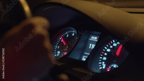 Close up dashboard lights up inside the dark interior of a car while driving at night.