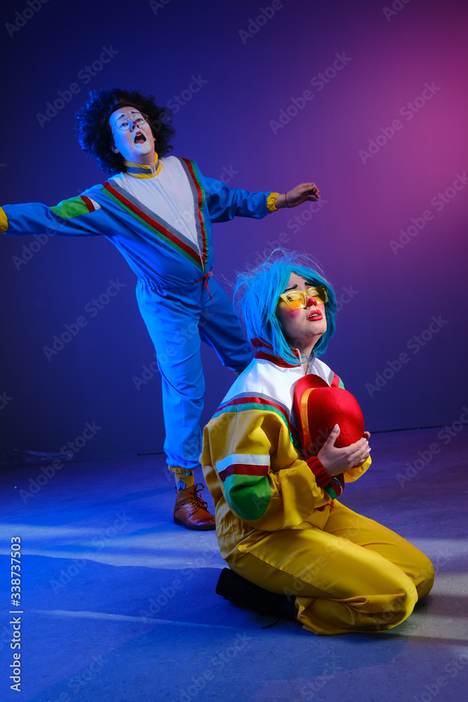 Fototapeta premium Two clowns a man and a woman with makeup in bright colored tracksuits in the style of the 80s.