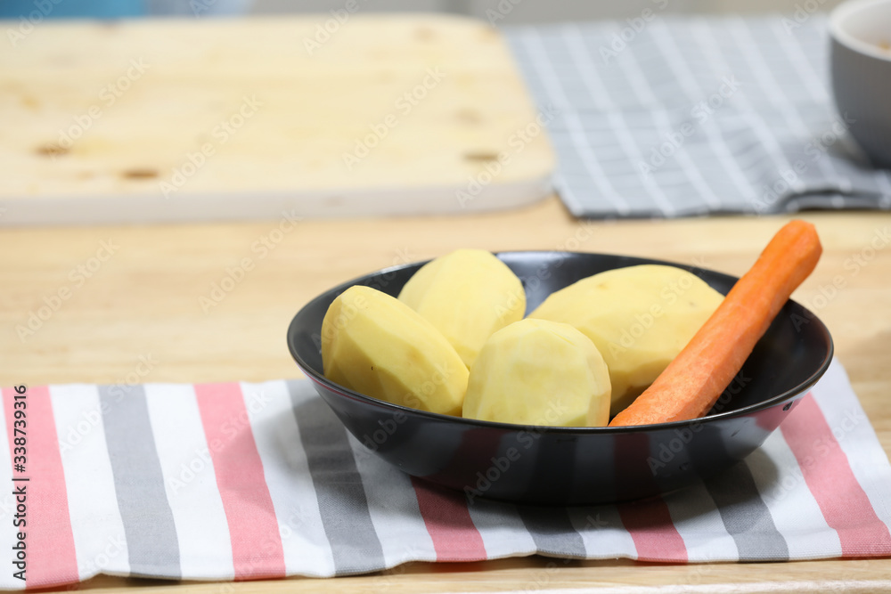 fresh peeled potatoes and carrot in a black plate with kitchen towel on a wooden table. Vegetarian breakfast . Vegan lunch. Vegetarian lunch. fresh peeled potatoes and carrot in a black plate with kitchen towel on a wooden table. Vegetarian breakfast . Vegan lunch. Vegetarian lunch.