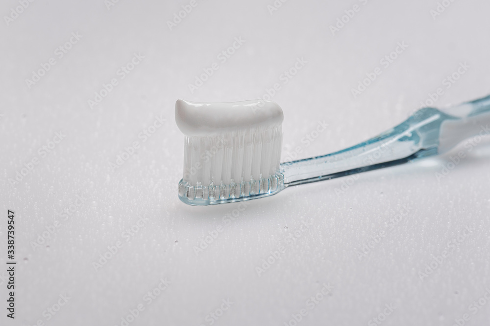 white toothbrush with smeared toothpaste on the bristles on a wet white background with water drops white toothbrush with smeared toothpaste on the bristles on a wet white background with water drops