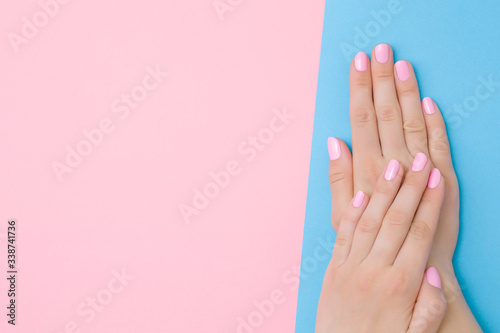 Beautiful groomed woman hands with light pink nails on pastel blue table side. Two colors background. Closeup. Manicure, pedicure beauty salon concept. Empty place for text or logo. Top down view.