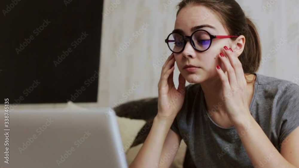 Exhausted female student using eye drops during study from home. Low angle of young tired woman in eyeglasses using laptop during distance learning and applying drops for treatment of dry eyes Exhausted female student using eye drops during study from home. Low angle of young tired woman in eyeglasses using laptop during distance learning and applying drops for treatment of dry eyes