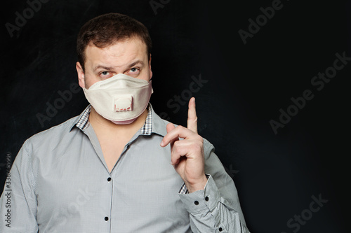 Man in medical mask pointing finger up on blackboard with copy space