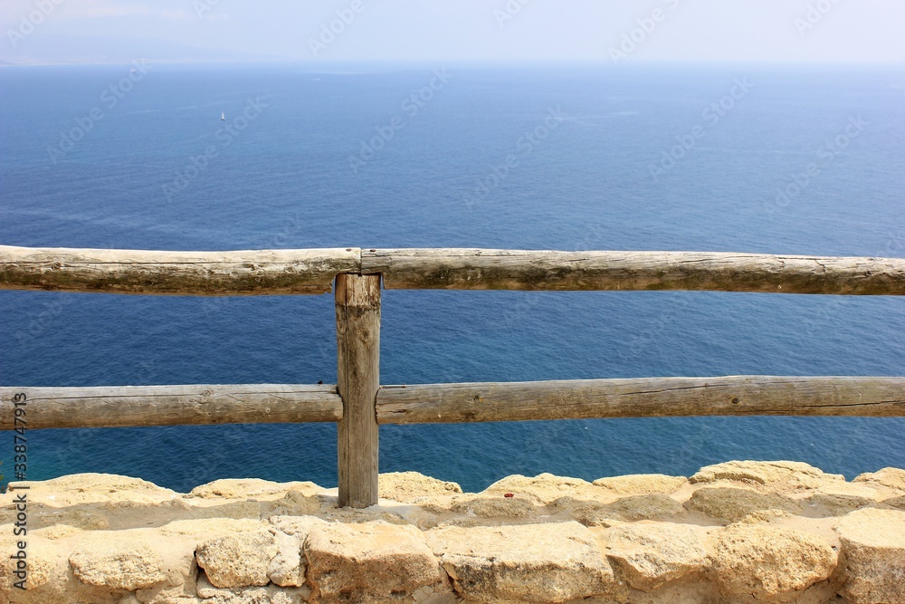 wooden low fence with a stone base on a background of blue sea and sky wooden low fence with a stone base on a background of blue sea and sky