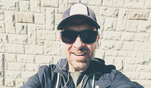 Man in sunglasses and a baseball cap listens to music on headphones and doing a selfie - Strong sunlight - Wide angle lens