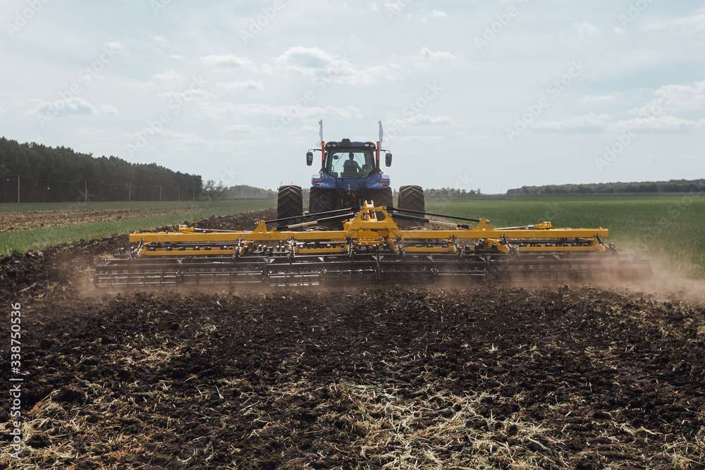 Fototapeta premium blue tractor in the field harrowing the land with a plow while driving