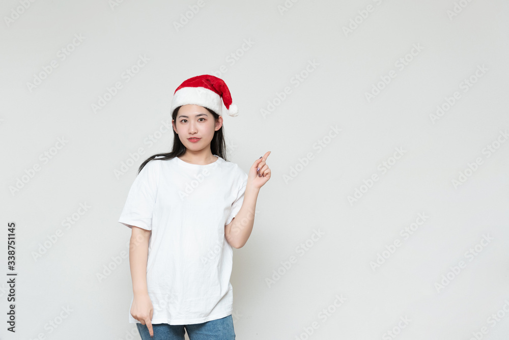 A young asian woman in a Christmas hat stands in front of the white wall