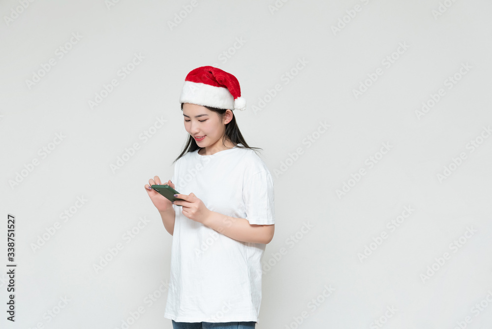 A young asian woman in a Christmas hat stands in front of the white wall