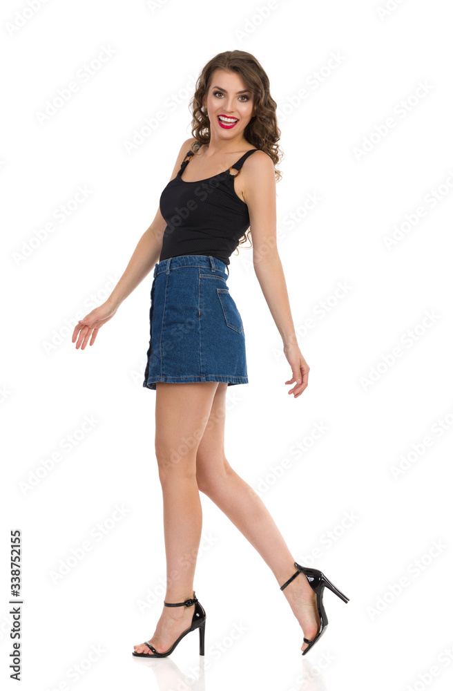 Young Woman In Jeans Mini Skirt And High Heels Is Walking And Talking. Side View. Young Woman In Jeans Mini Skirt And High Heels Is Walking And Talking. Side View.