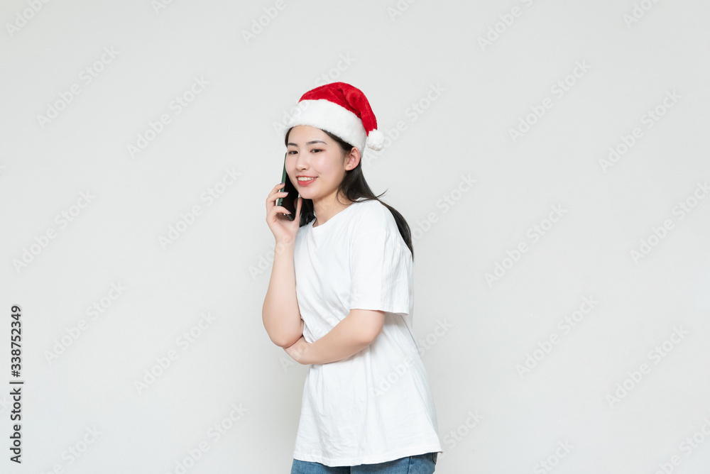 A young asian woman in a Christmas hat stands in front of the white wall