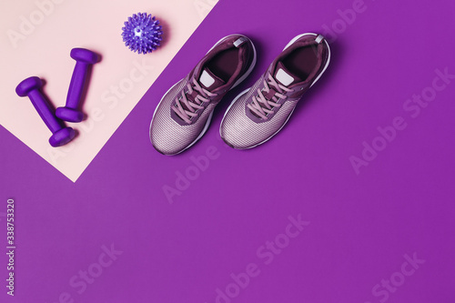 Sports flat-lay with sneakers, dumbbells and headphones on purple background.