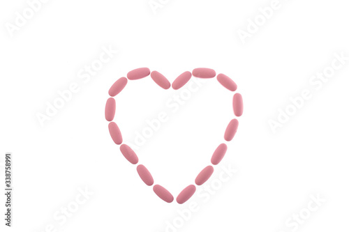 Pink pills in the shape of a heart on a white isolated background. Daily Vitamins dose. Heart shape made of tablets for therapy, concept of treatment and health care. Copy space.