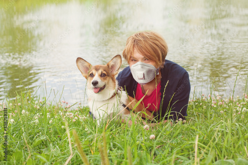 Happy older woman in medical mask and her dog outdoors (woman 60 years old)
