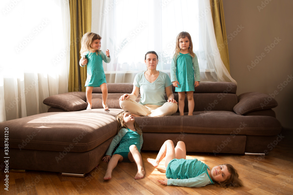 Mom meditates sitting on a sofa And her little daughter plays in the room. а lot of children. Living with a child in quarantine. stay home concept Mom meditates sitting on a sofa And her little daughter plays in the room. а lot of children. Living with a child in quarantine. stay home concept