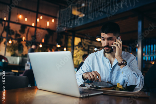 man using laptop and talking on mobile phone while having lunch in restaurant