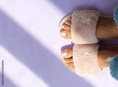 female legs with gentle white nails in home fur fluffy pink slippers on on a light background with sunlight. flat lay. Top view. The concept of a cozy bright girl house. copy space. Housewife concept. photo