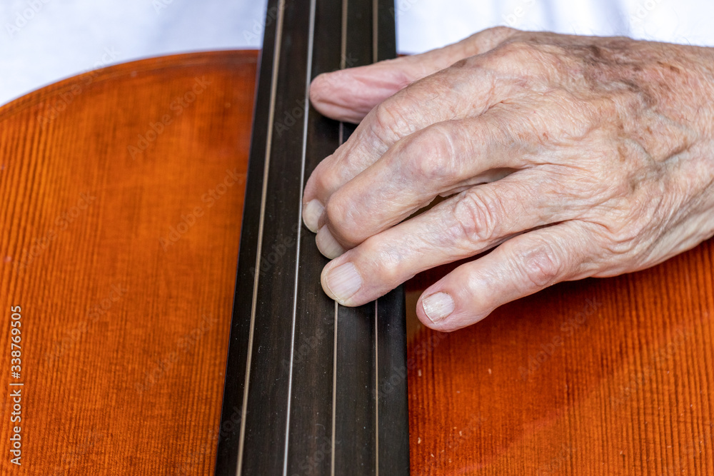 Alte, knochige Hand auf Saiten eines Cellos Alte, knochige Hand auf Saiten eines Cellos
