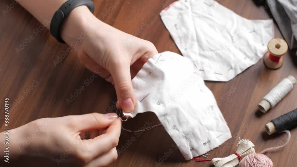 Young woman sews from white cotton fabric at night in the house. Making your own reusable protection masks. Close-up view of a woman's hands. Time lapse fast footage Young woman sews from white cotton fabric at night in the house. Making your own reusable protection masks. Close-up view of a woman's hands. Time lapse fast footage