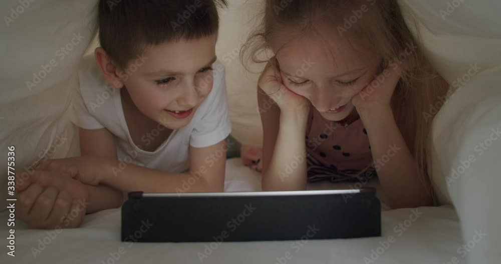 boy and girl lying under blanket with tablet boy and girl lying under blanket with tablet