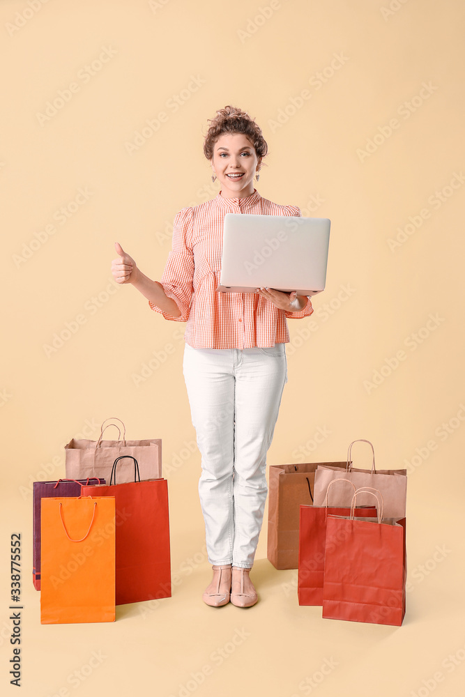 Beautiful young woman with laptop and shopping bags on color background Beautiful young woman with laptop and shopping bags on color background