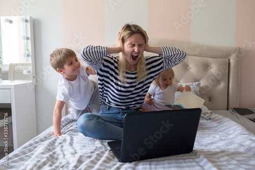 Mother working from home with kids. Quarantine and closed school during coronavirus outbreak. Children make noise and disturb woman at work. Homeschooling and freelance job. Boy and girl playing.