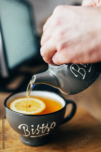 A man pours tea from a ceramic teapot into a ceramic cup - a tea break when working in the office at the computer table