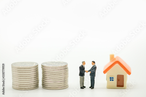 Two businessman miniature people figures meeting and hand shake with many stack of silver coins and mini home on white background with copy space. Using as business, financial, money and cooperation c
