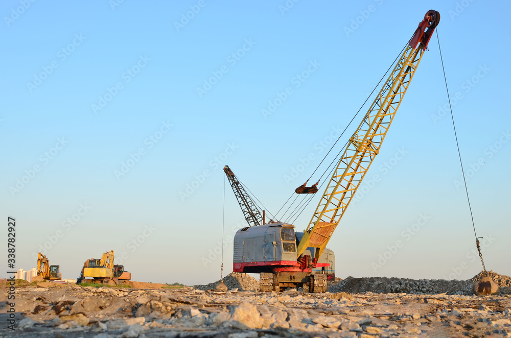 Large crawler crane or dragline excavator with a heavy metal wrecking ball on a steel cable. Wrecking balls at construction sites. Dismantling and demolition of buildings and structures Large crawler crane or dragline excavator with a heavy metal wrecking ball on a steel cable. Wrecking balls at construction sites. Dismantling and demolition of buildings and structures