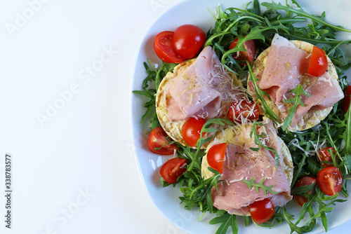 Concetto di cibo sano. Gallette di mais biologiche con prosciutto, insalata di rucola fresca e pomodori su un piatto, sfondo bianco. Vista dall'alto.