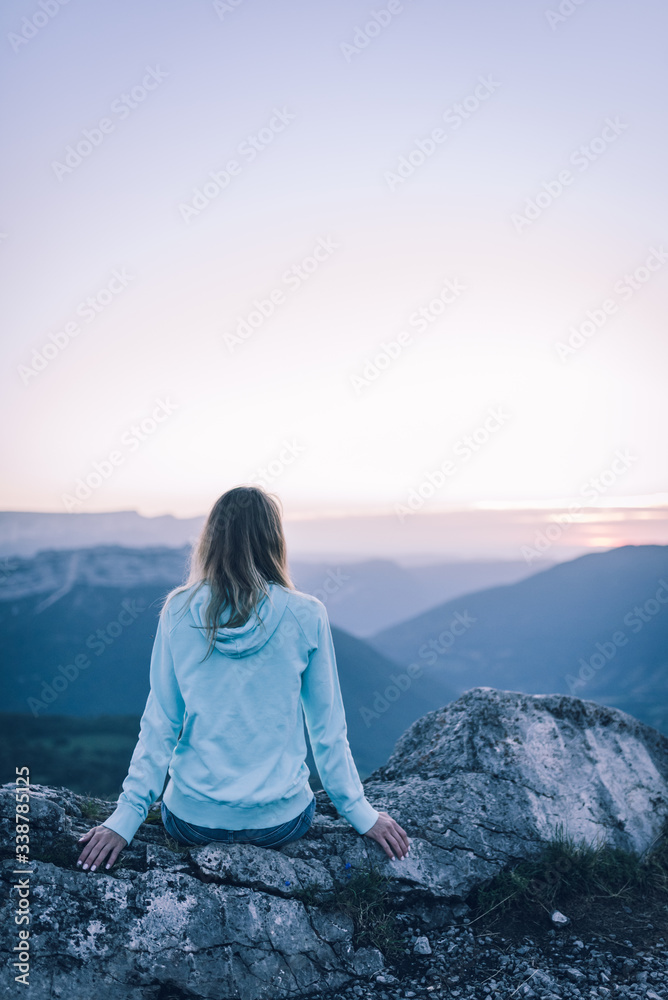 Femme du dos assise sur le rocher regarde le coucher du soleil à la monagne