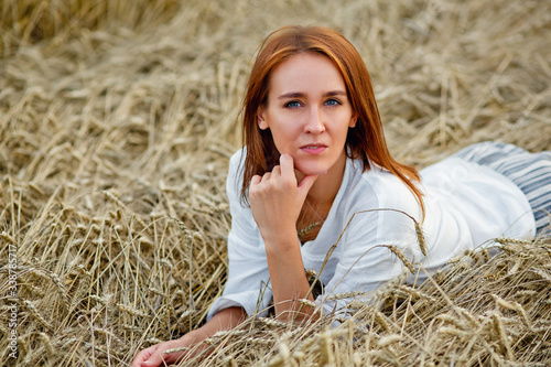 Girl lying in a wheat field and posing on hay dry grass, summer season. Relaxing in nature. Young woman posing in field